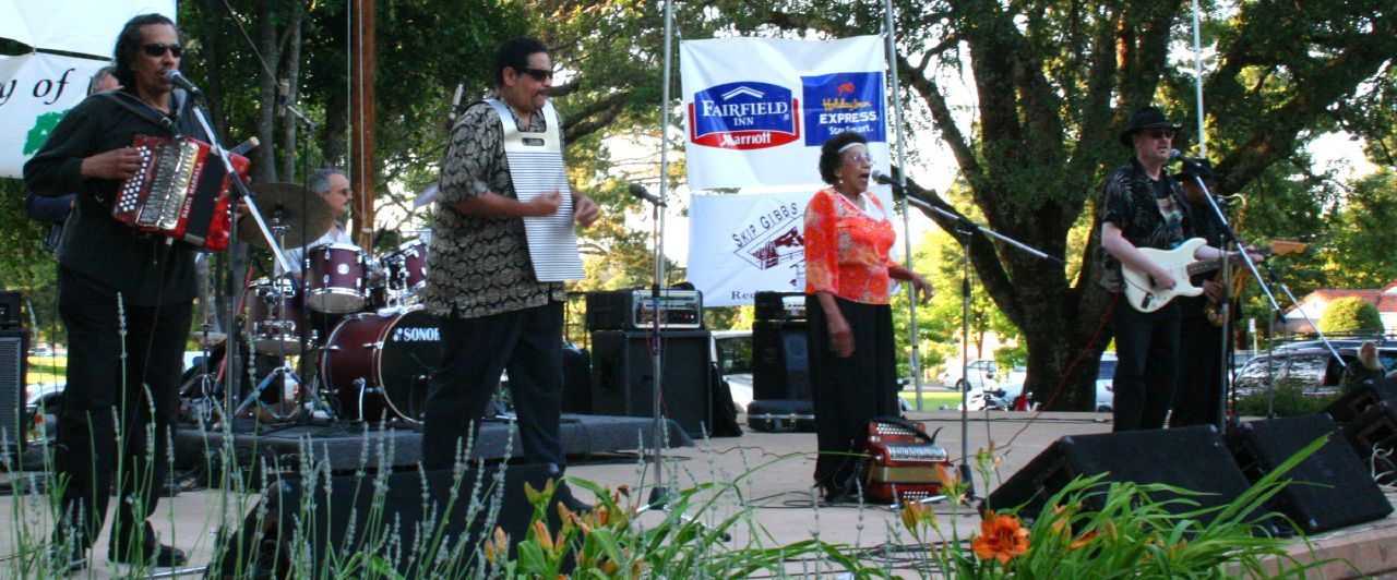 Four musicians perform on an outdoor stage with instruments and microphones. - Todd Grove Park – Tiger Stadium loop from Ukiah