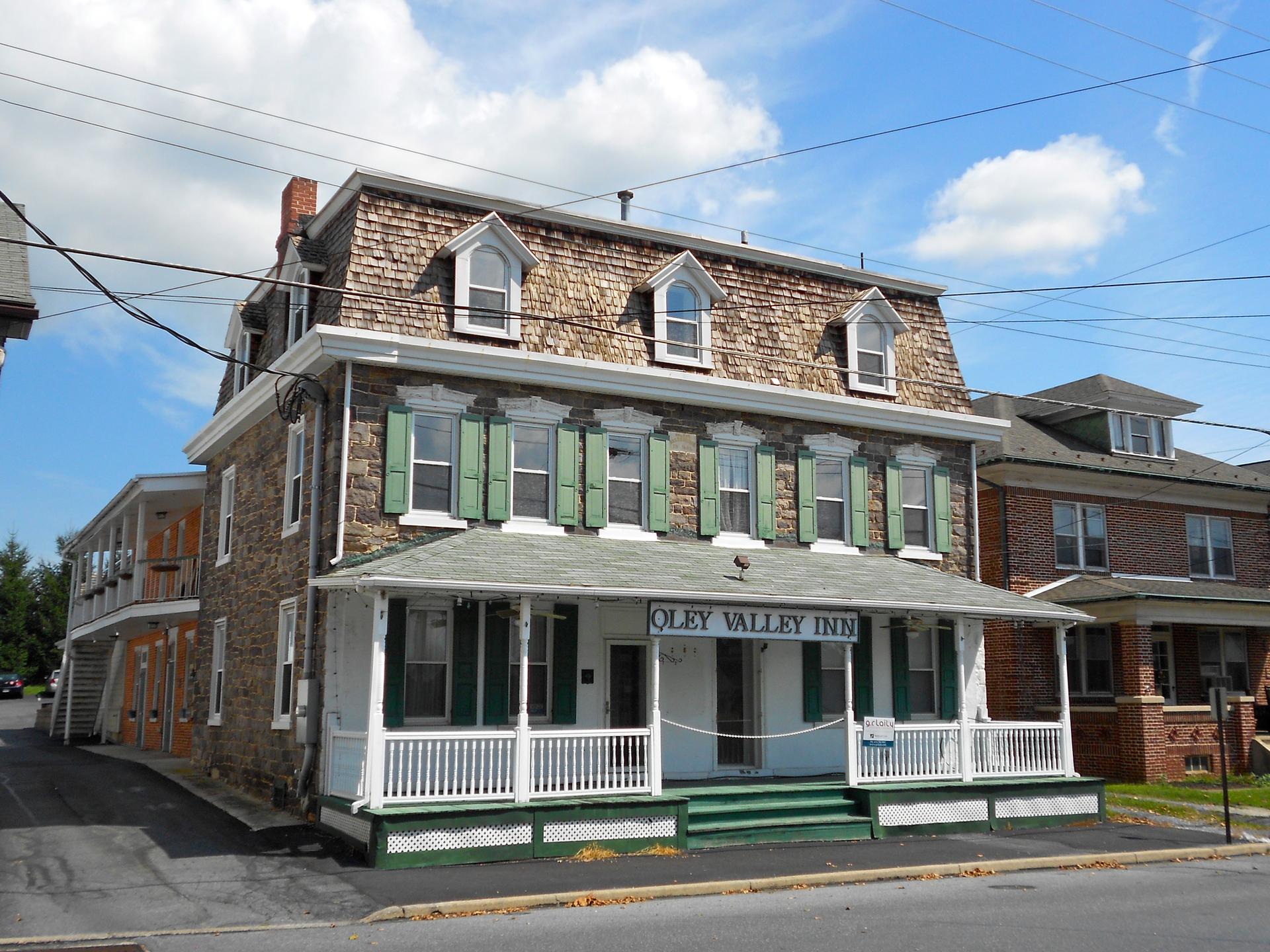 A large stone building with green shutters and a porch under a cloudy sky.
