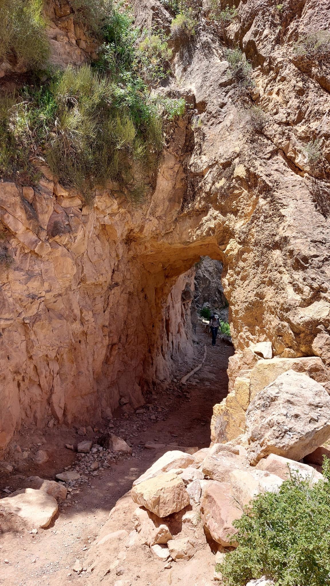 A person walks through a carved rock tunnel on a dirt path.