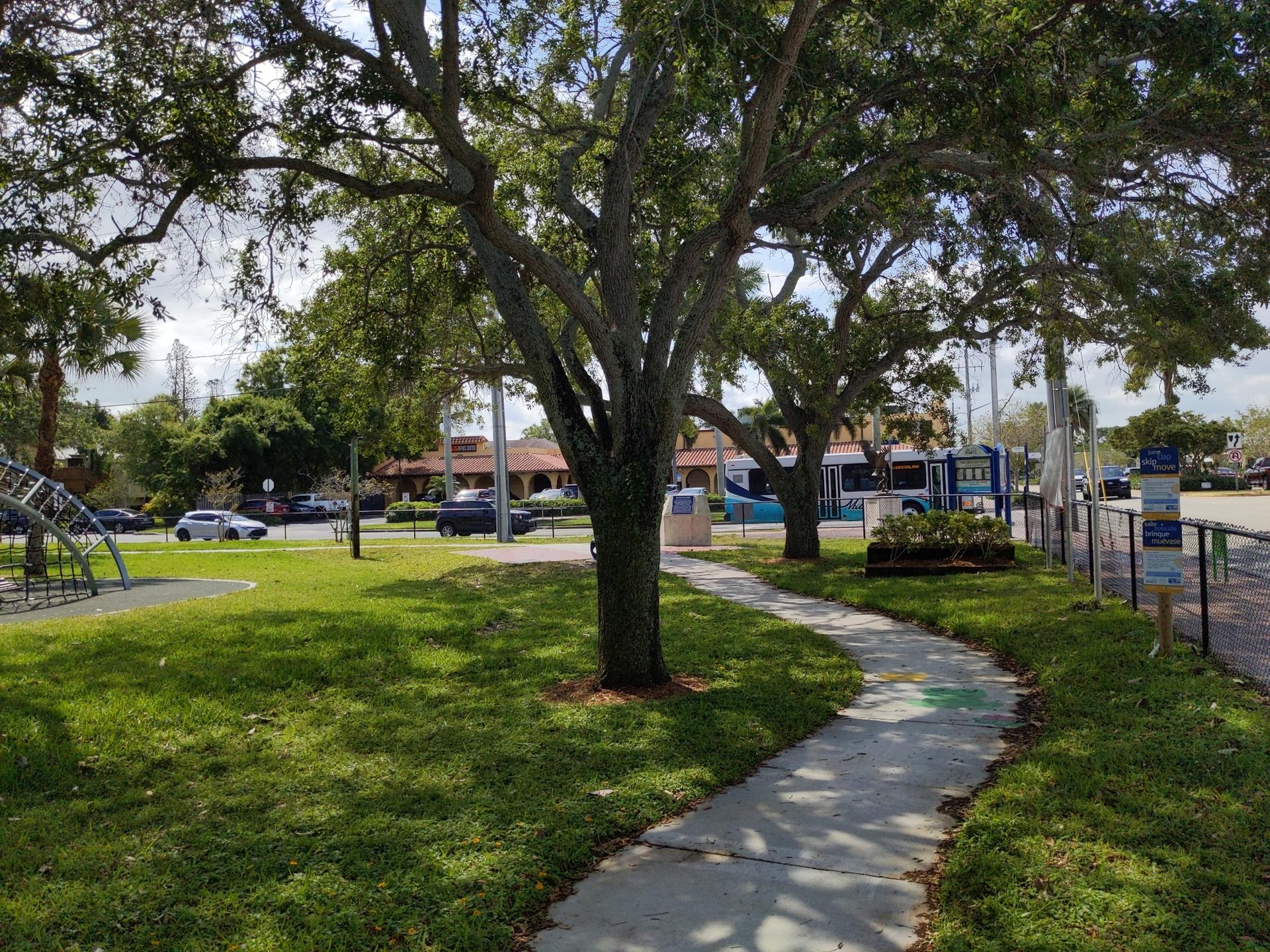 A winding paved path through a sunny park with large trees.