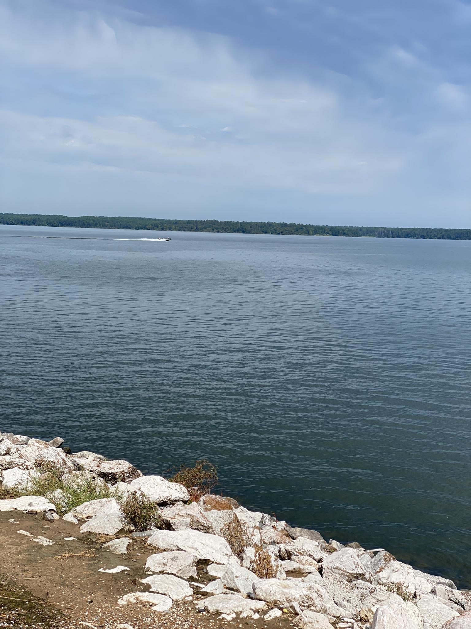 Vast lake with rocky shore, distant boat, and cloudy sky.