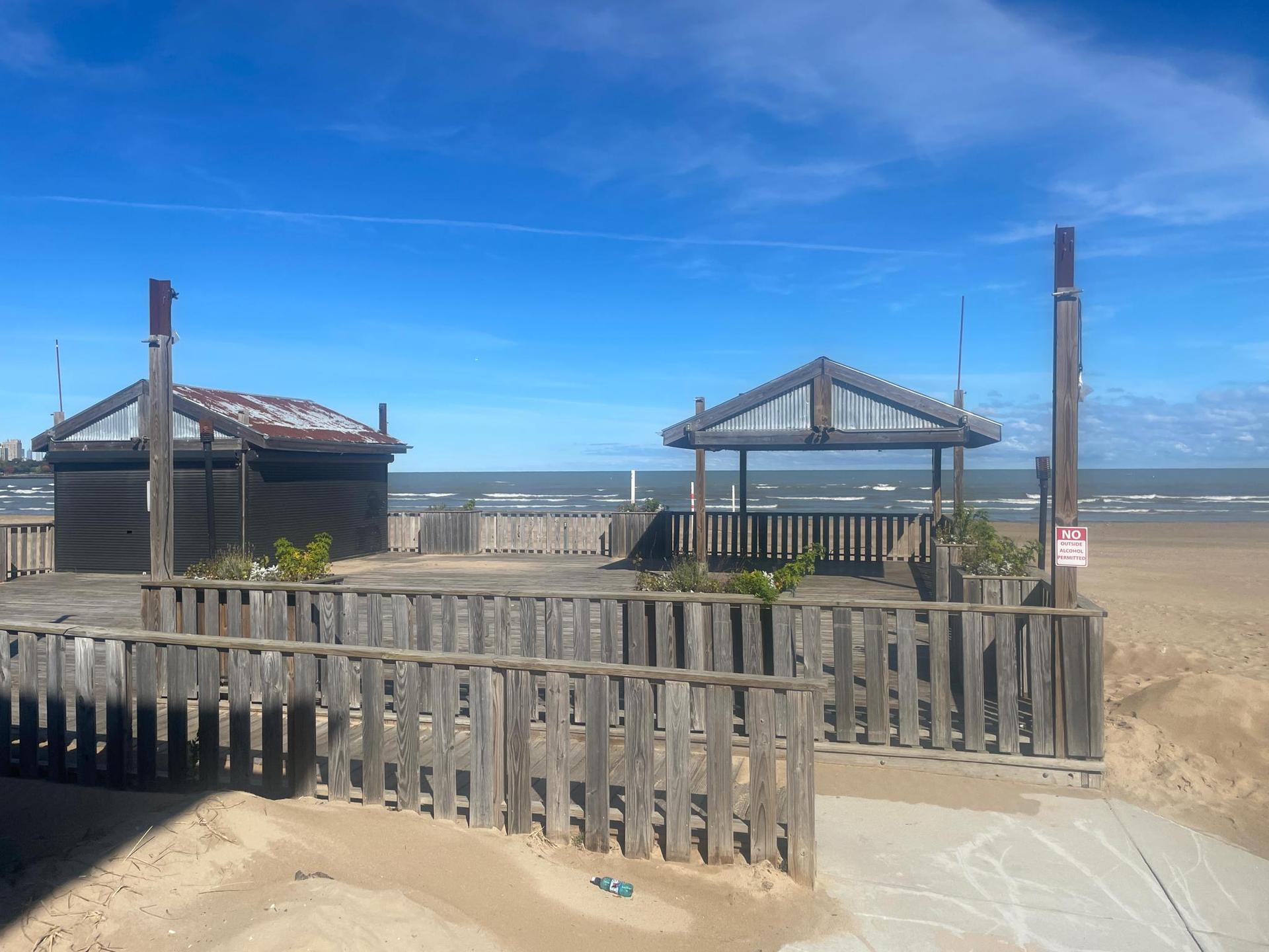 Two wooden structures on a sunny beach next to the ocean under blue sky.