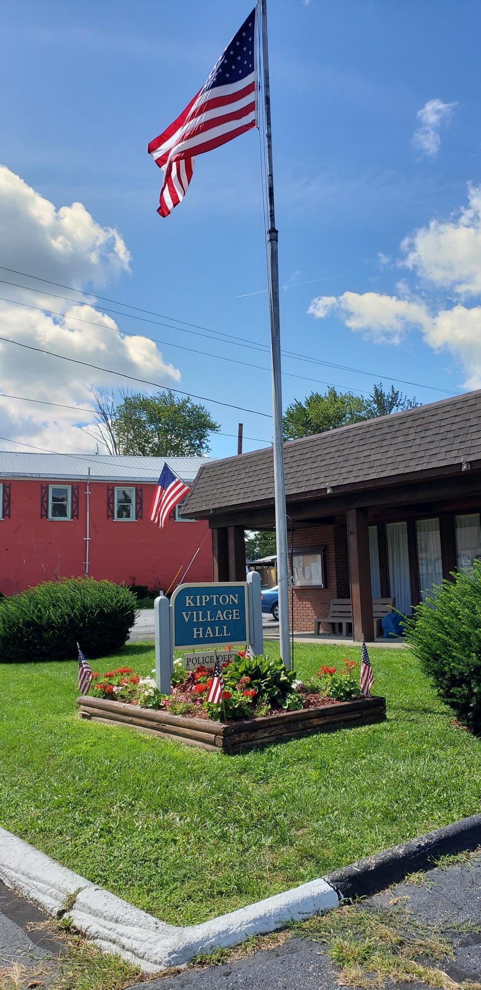 American flag flying high above a sign and buildings on a sunny day.