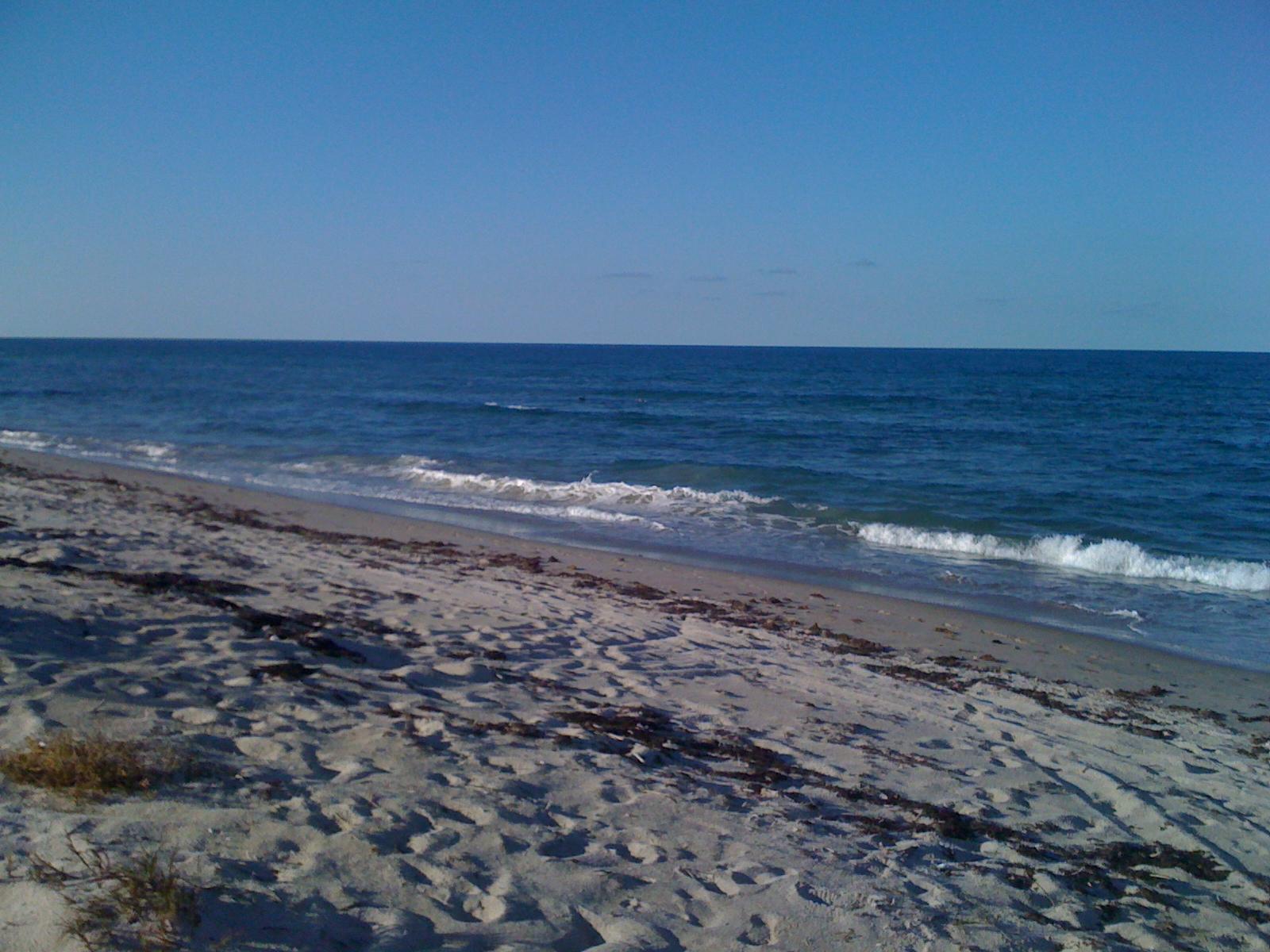 Ocean waves gently break on a sandy beach under a clear blue sky.