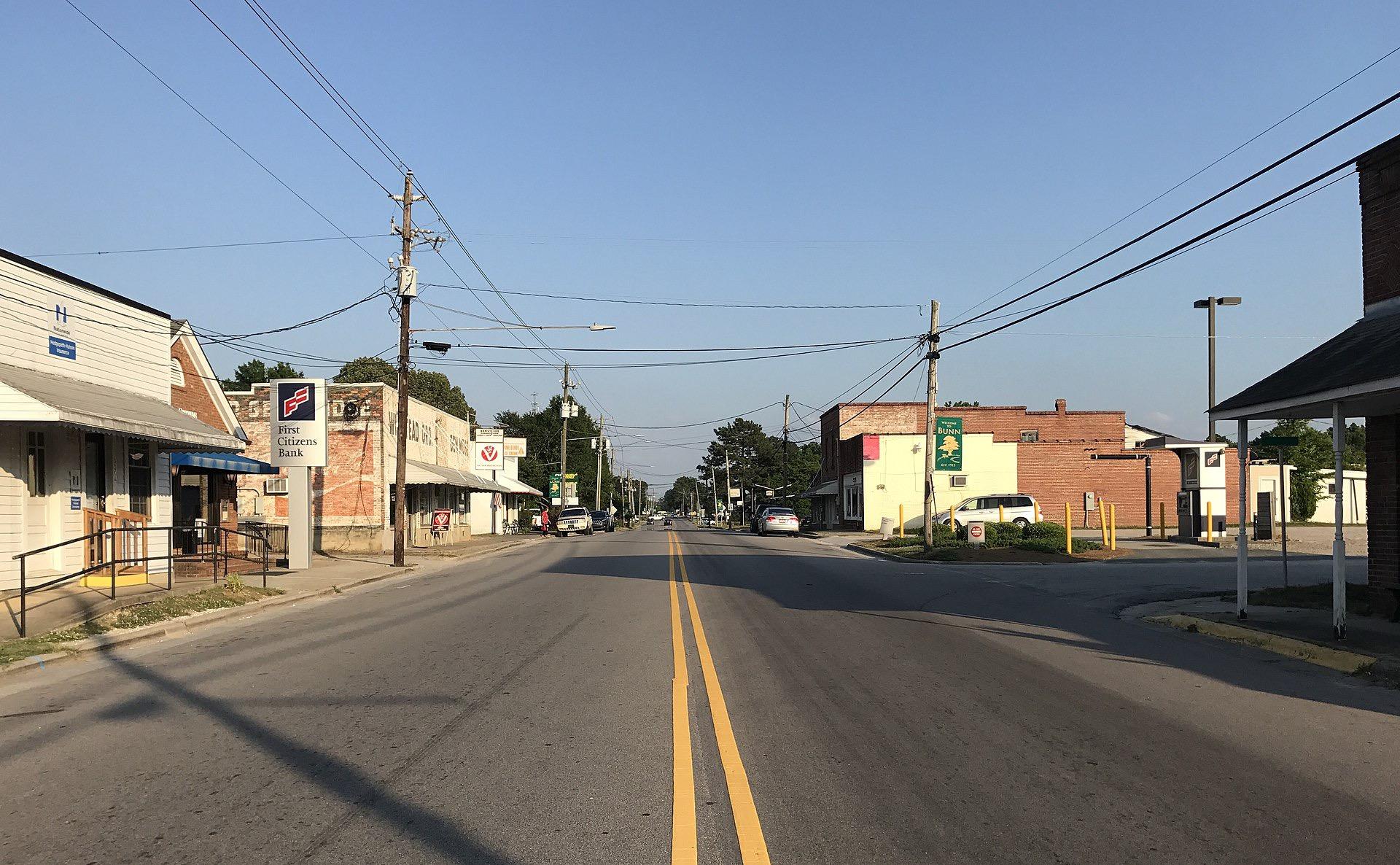 A sunny street scene with buildings, power lines, and parked cars.