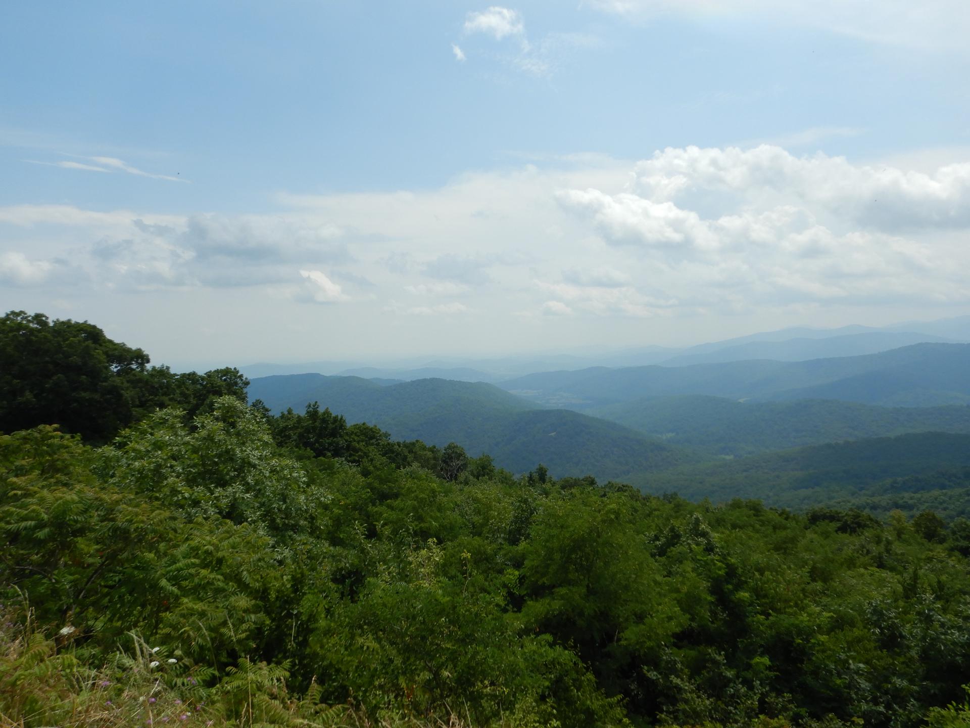 Panoramic view of multiple green mountain ranges under a partly cloudy sky.