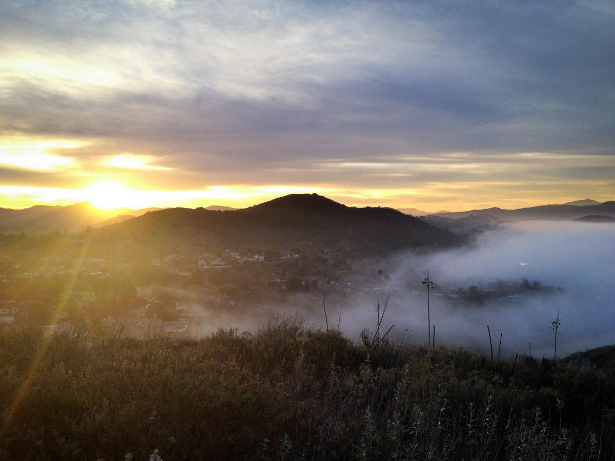 Golden sunrise over a misty valley, with mountains and clouds in the distance.
