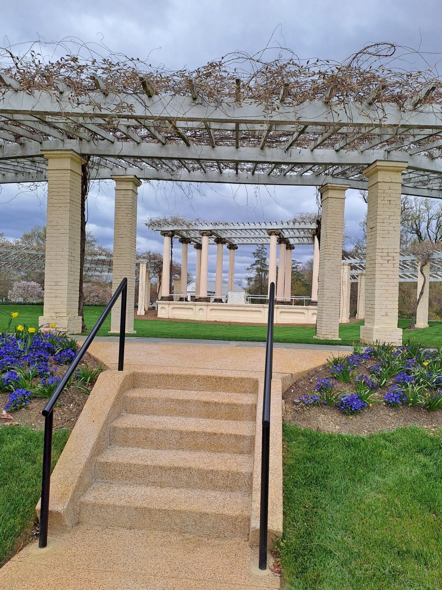 Stone steps leading to a large pergola with distant classical structures.