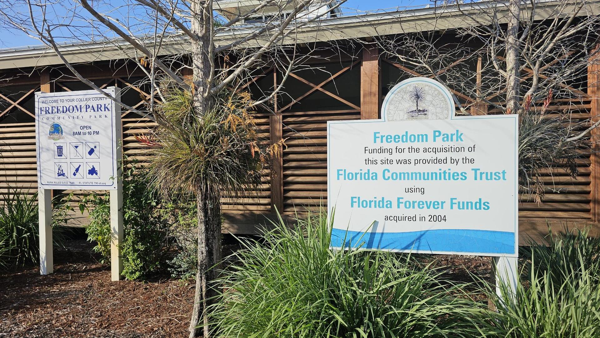 Two white informational signs stand in front of a wooden building on a sunny day.