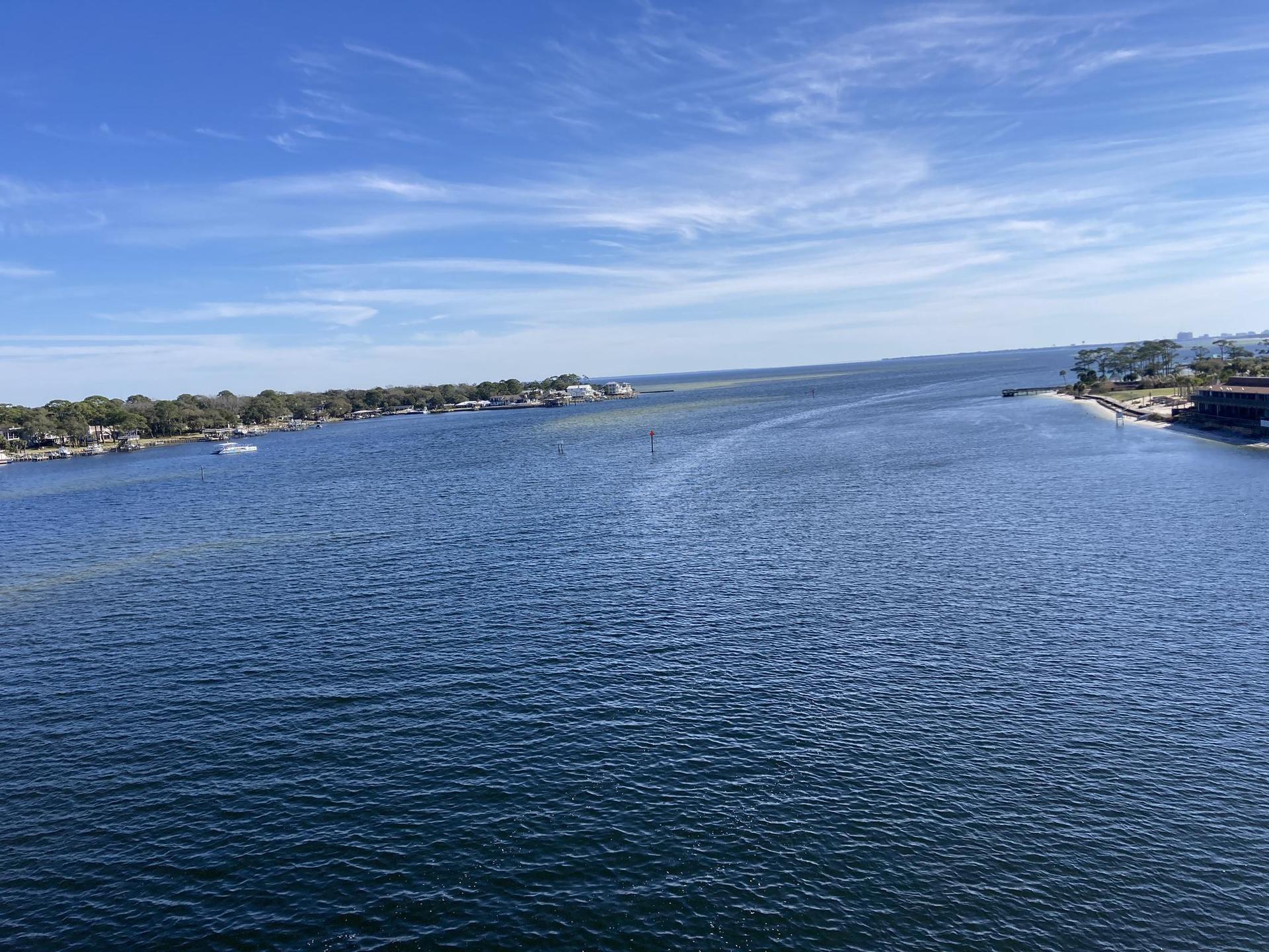 Wide blue waterway under a clear sky, with distant land and boats.