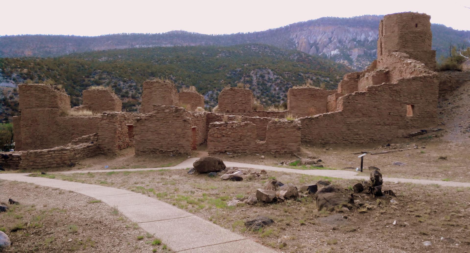 Ancient stone ruins with a path, under a soft sky, mountains in background.