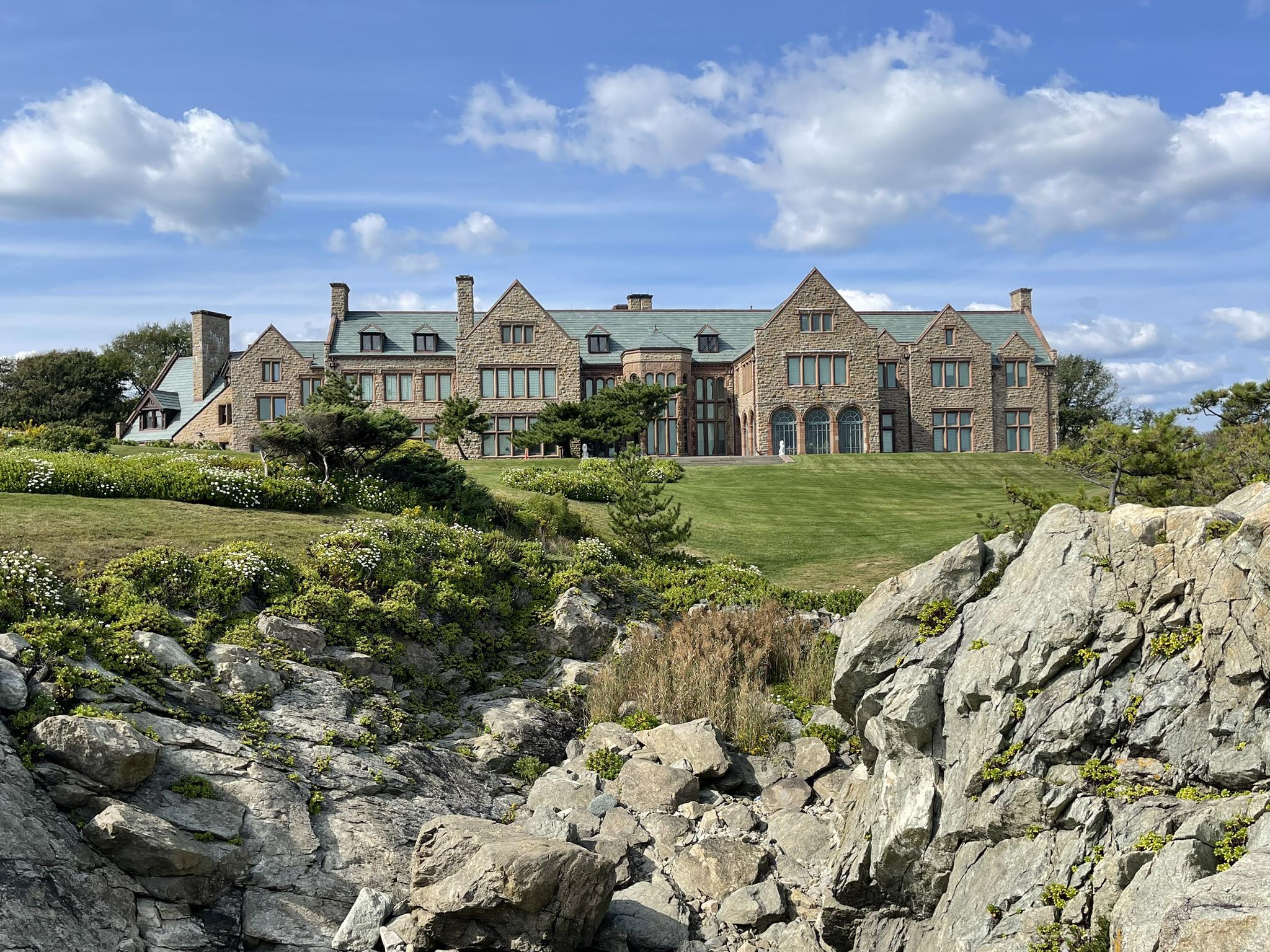 Grand house on a green hill, seen from a rocky foreground, sunny day.