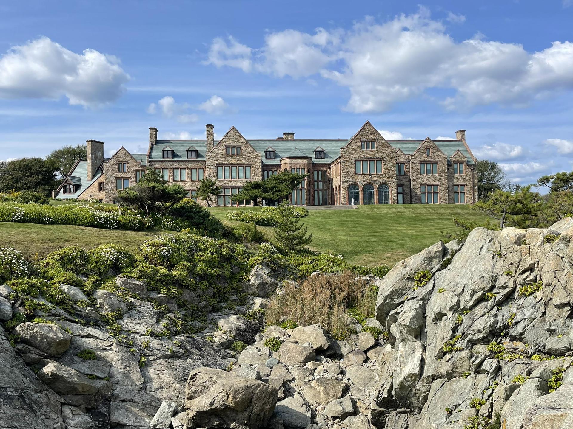 Grand house on a green hill, seen from a rocky foreground, sunny day.