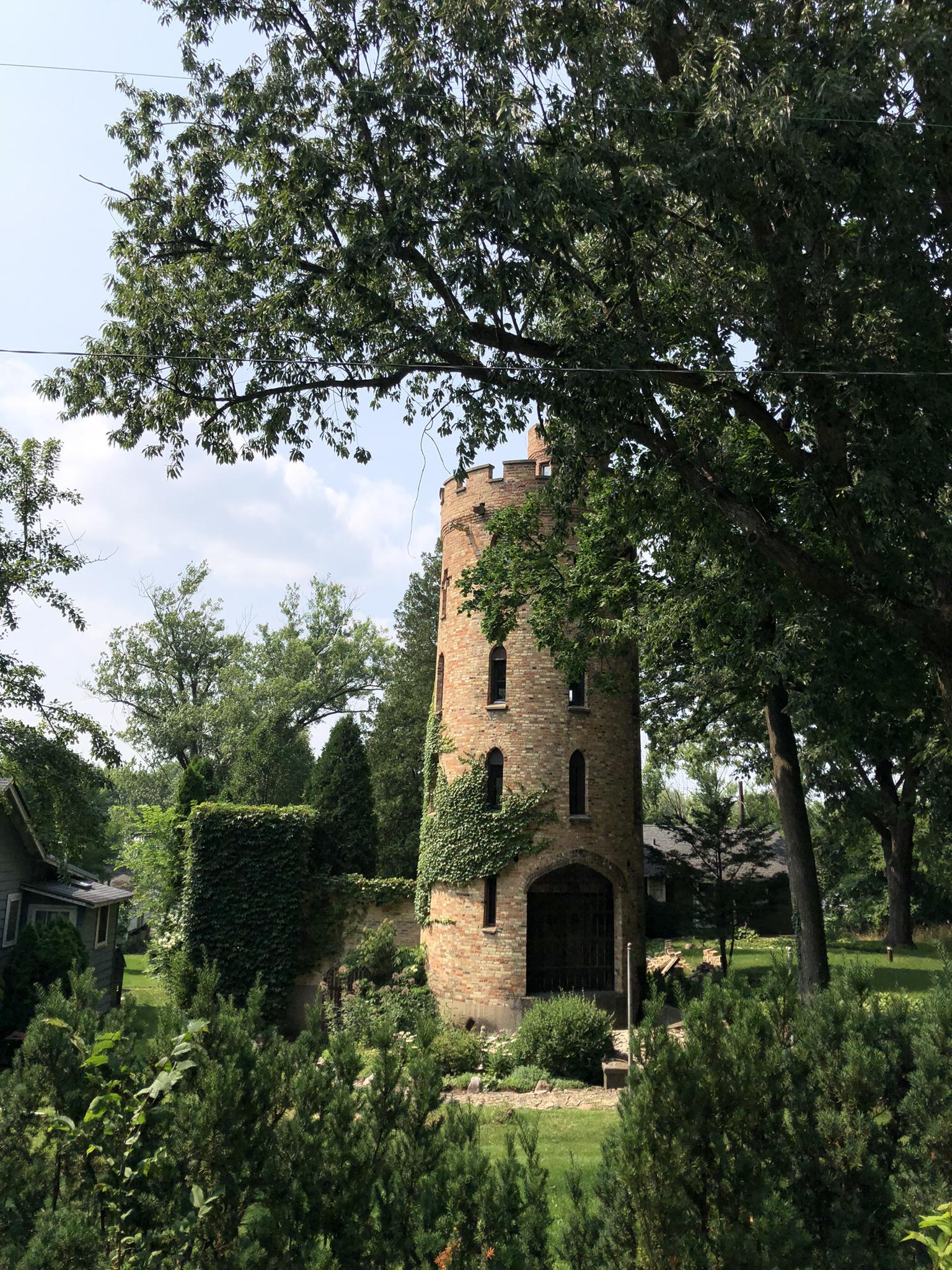 A tall, ivy-covered brick tower surrounded by lush green trees on a bright day.