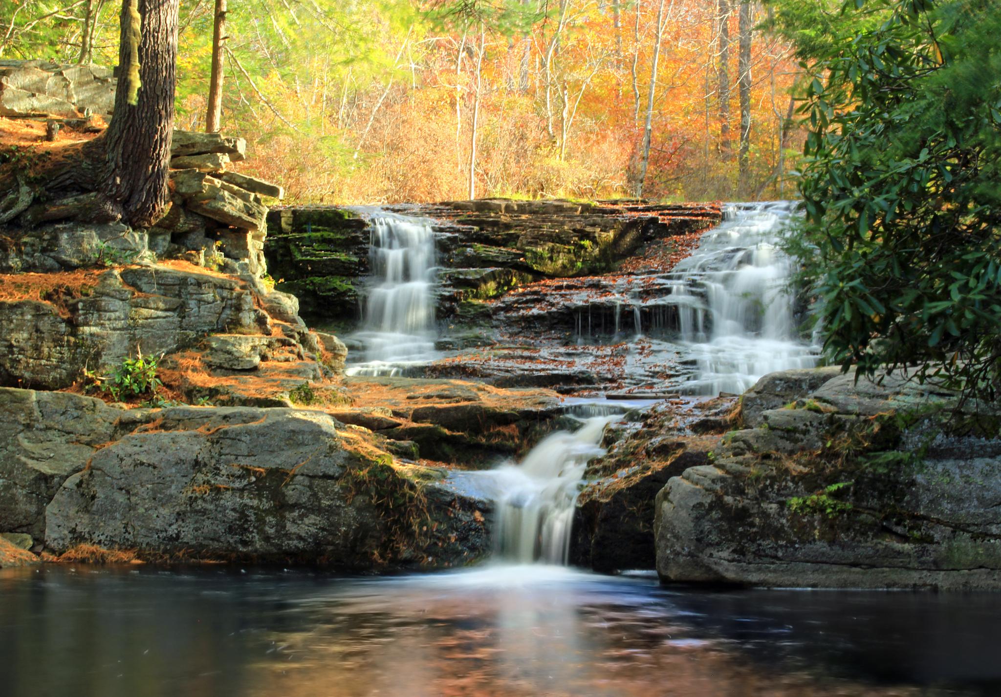 A multi-tiered waterfall cascades over rocks into a calm pool.