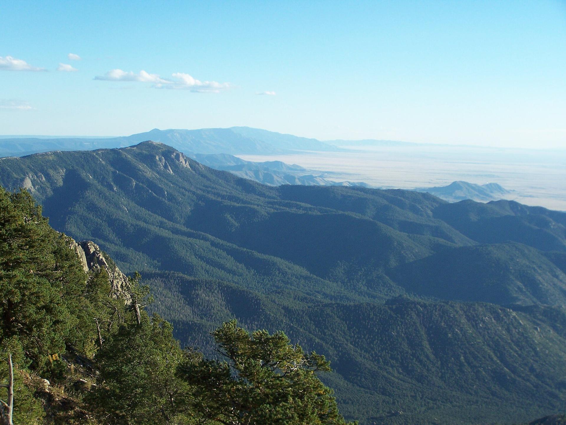 Expansive view of forested mountains and a hazy valley under a blue sky.