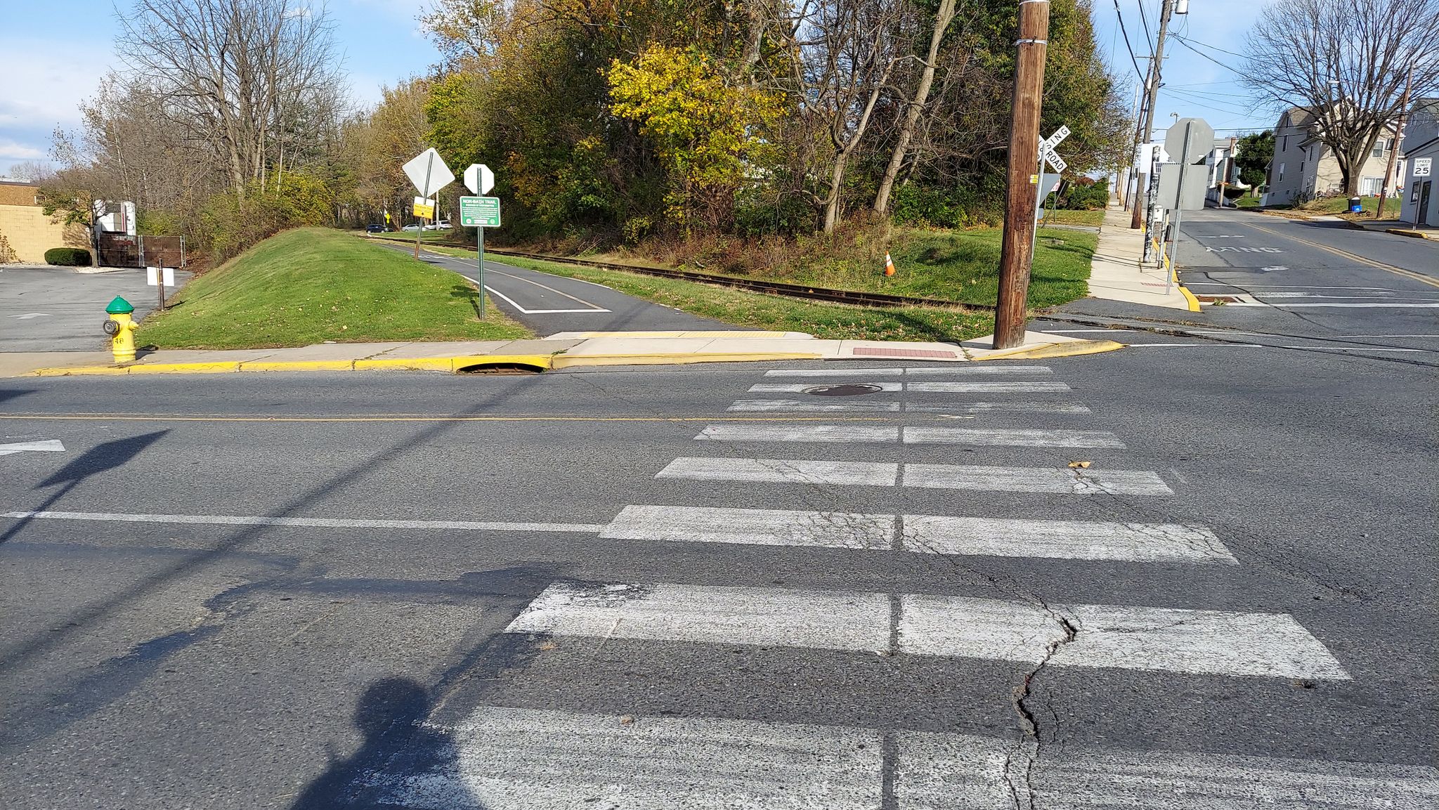 An empty street crosswalk under bright daylight, with autumn trees and buildings. - Nor-Bath Trail
