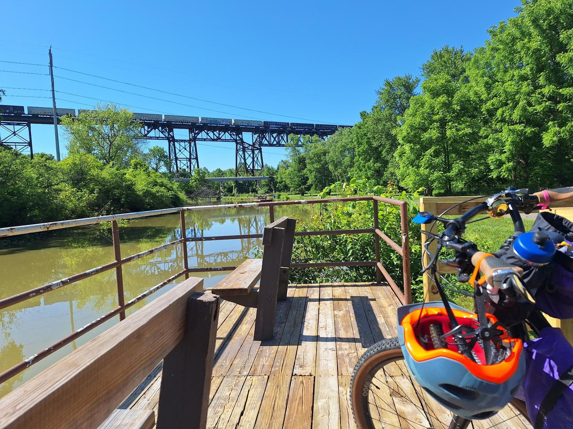 Bicycle on a wooden deck overlooking a river with a large bridge.