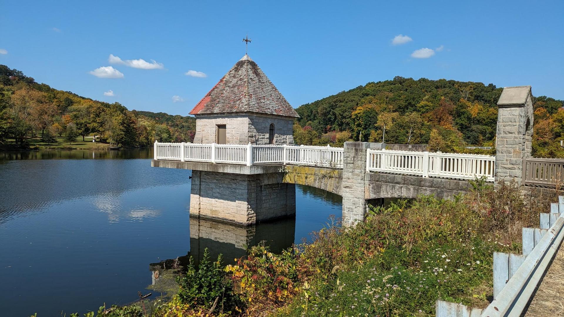 Stone building and bridge over a lake, surrounded by autumn hills on a sunny day.