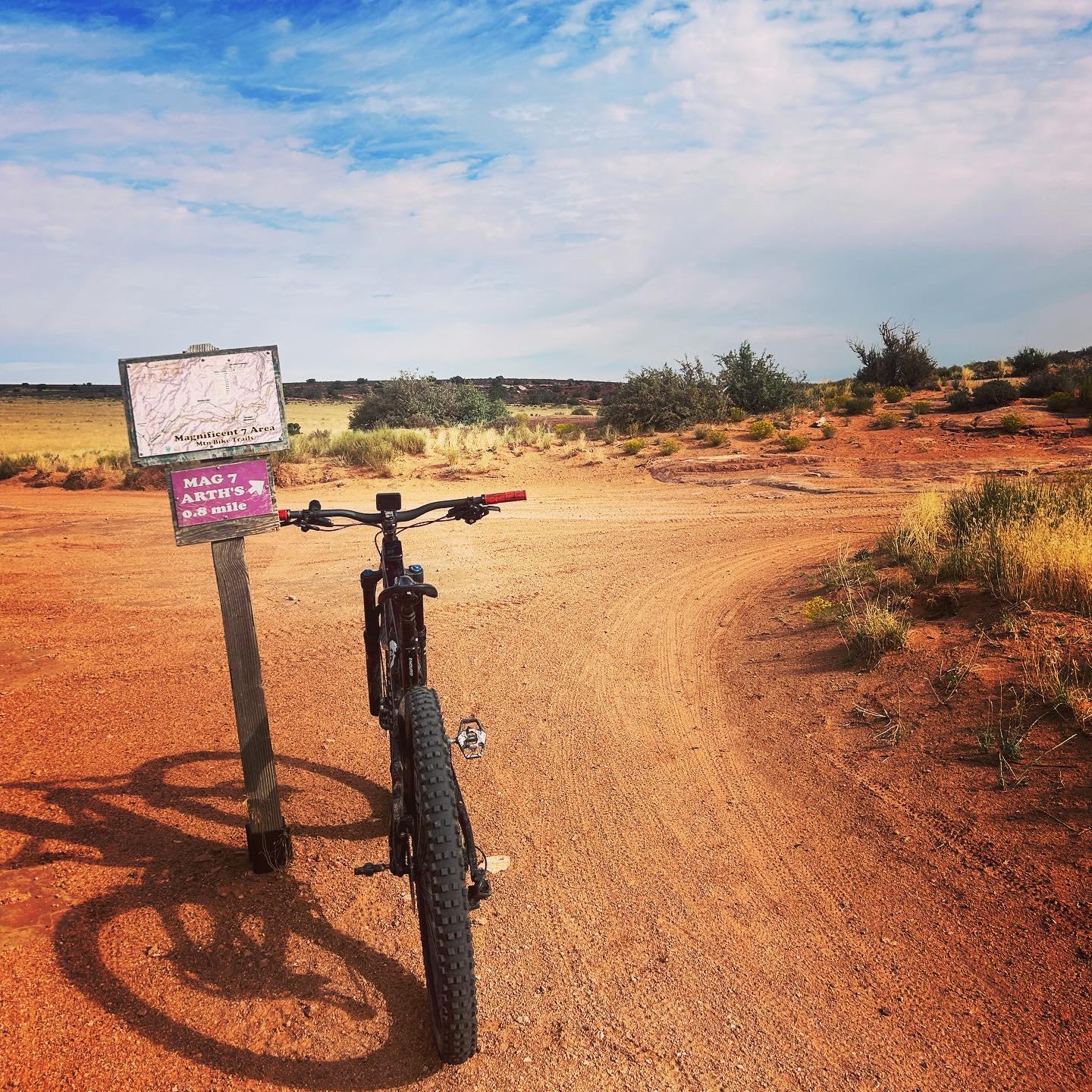 Mountain bike parked next to a trail sign on a dirt path under a bright sky.