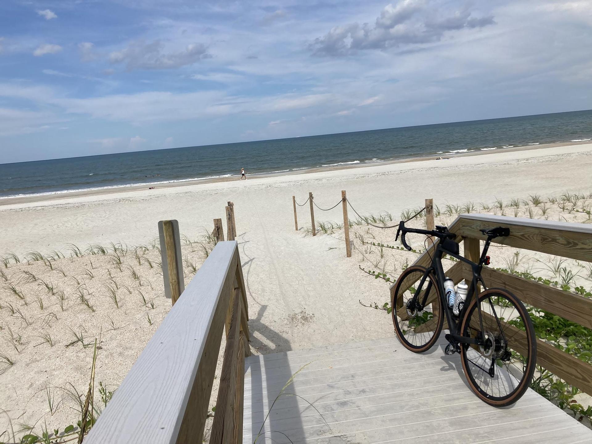 Bicycle parked on a wooden boardwalk overlooking a wide sandy beach and ocean.