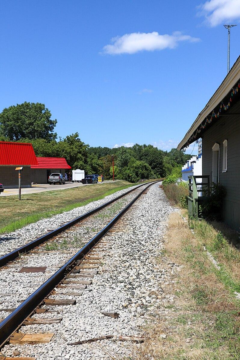 Railroad tracks run beside a building under a clear blue sky.