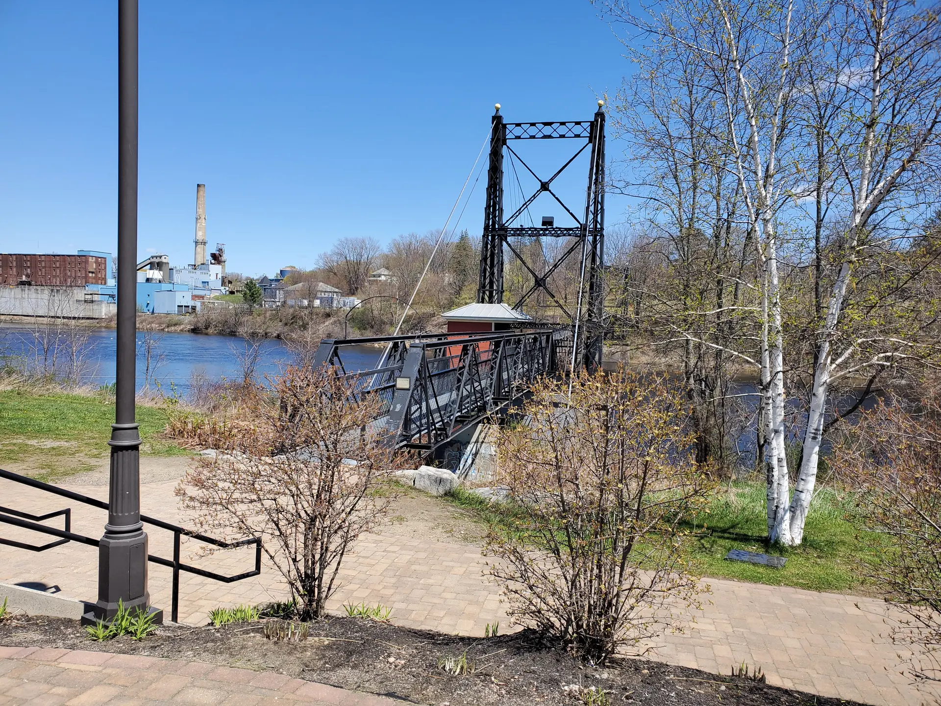 Black metal bridge spans a river on a bright, sunny day.
