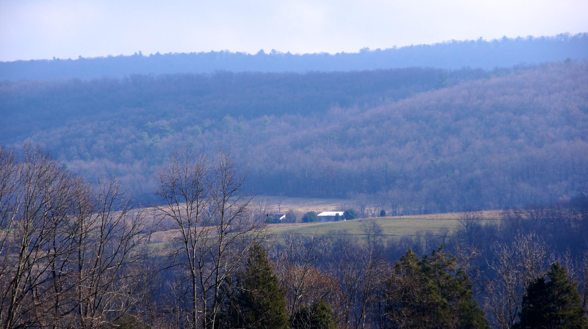 Hazy view of distant farm buildings in a valley surrounded by hills.