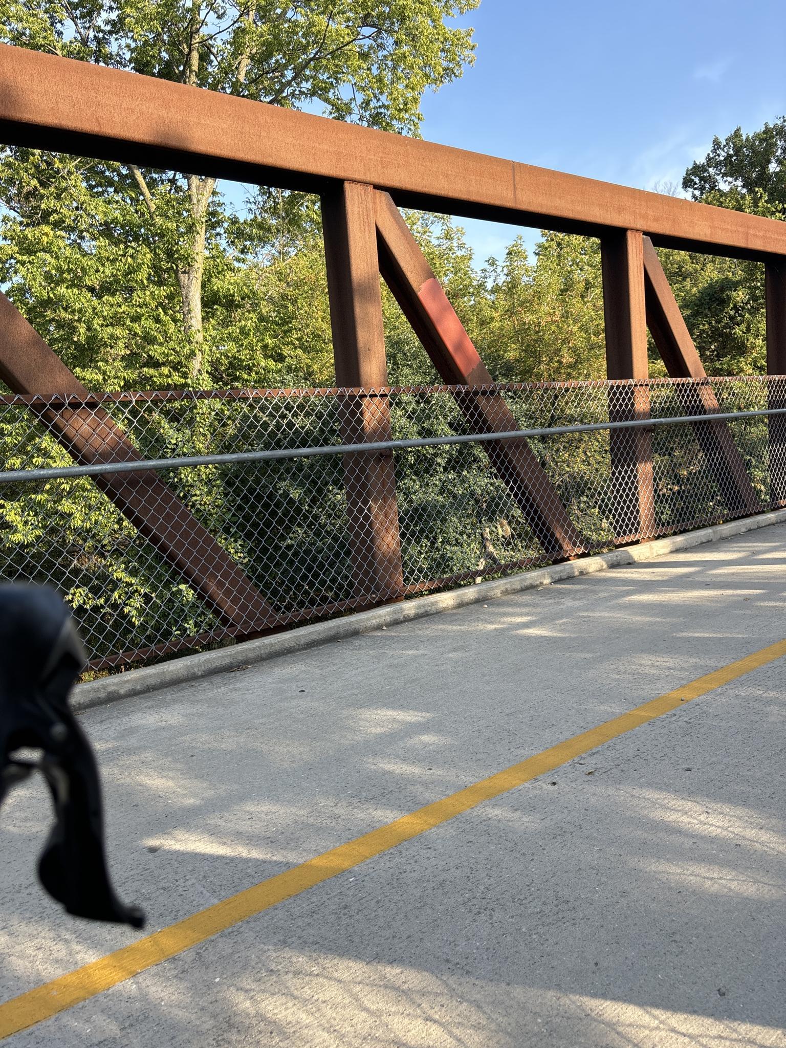 A bicycle on a paved bridge with a rusty metal truss structure.