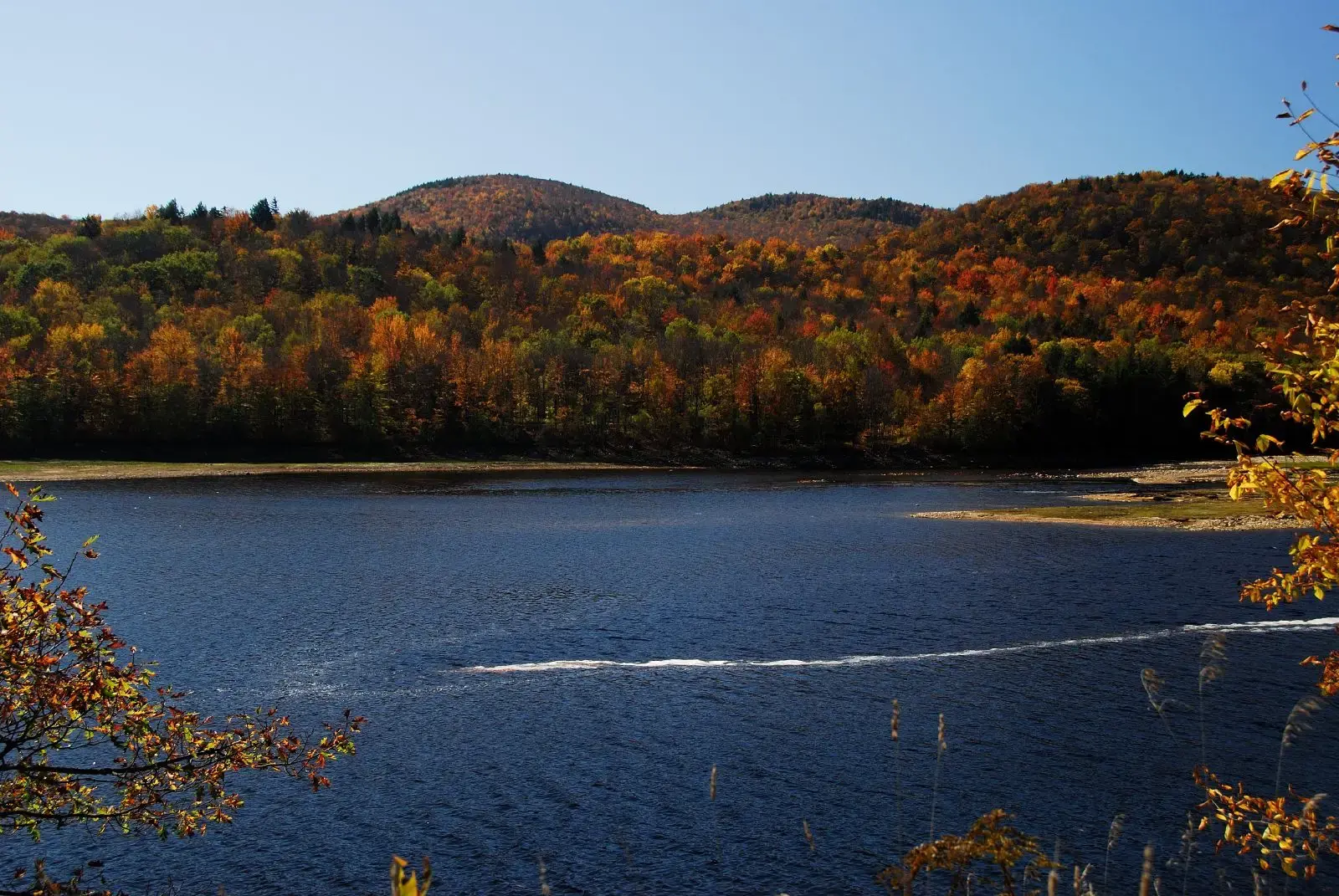 Blue lake with a boat wake, surrounded by colorful autumn forested hills.
