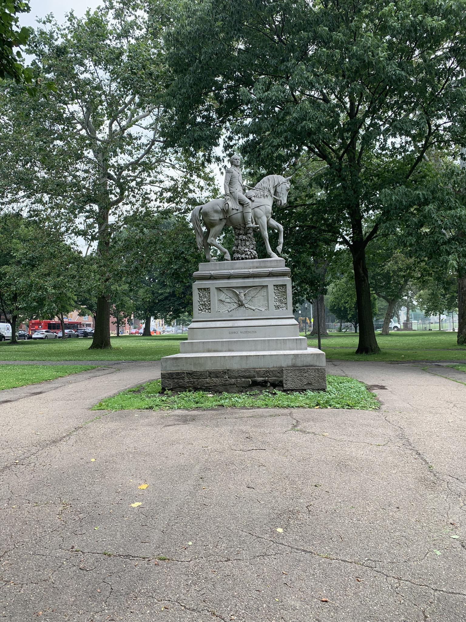 Equestrian statue in a park surrounded by tall green trees.