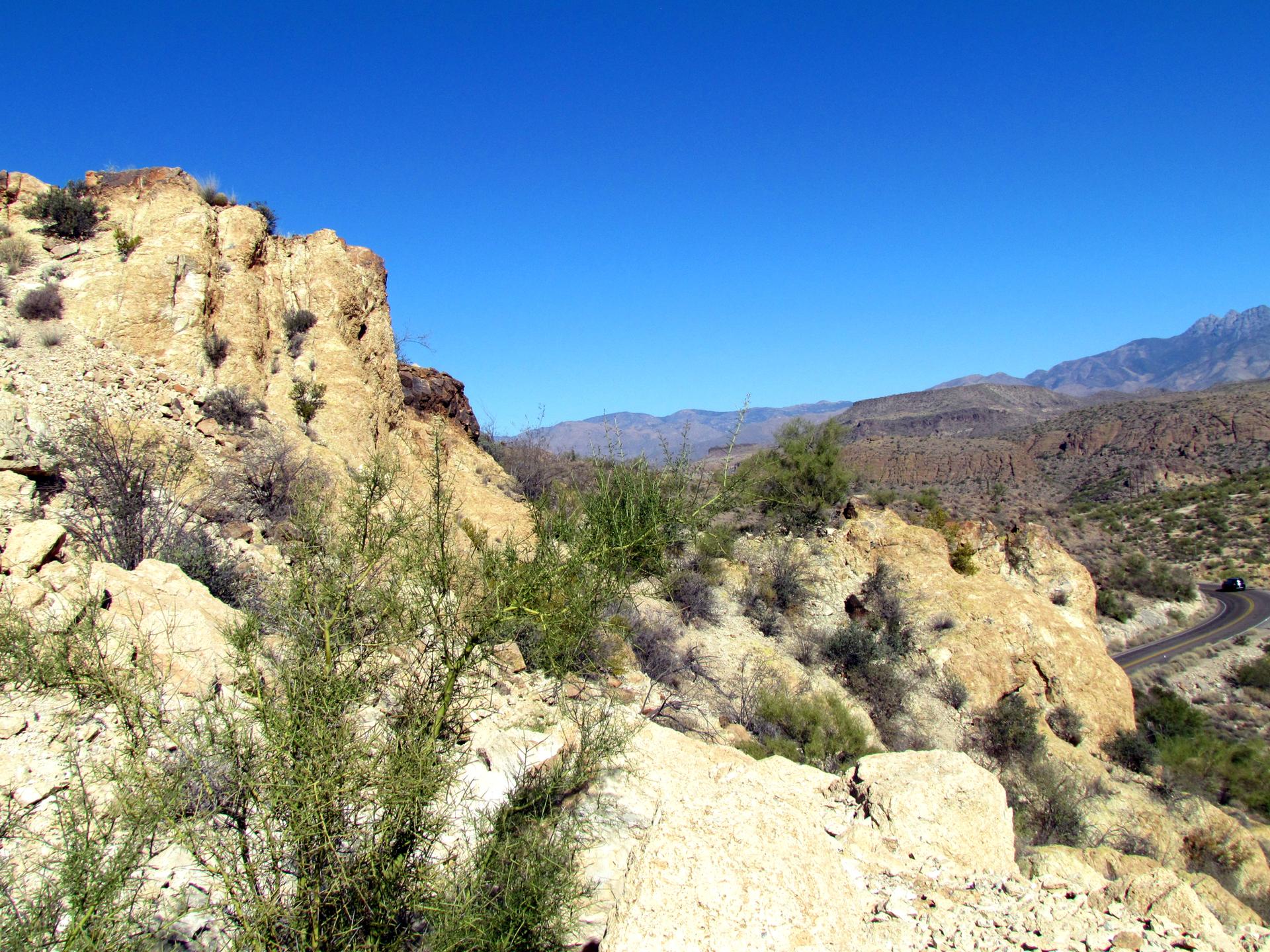 Rocky desert hills with sparse green vegetation and a winding road in daylight.