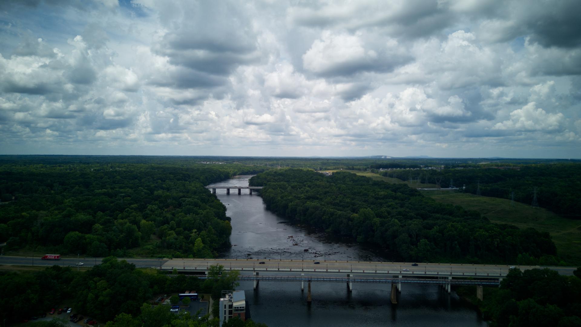 Aerial view of a wide river flowing through dense forest under cloudy skies.