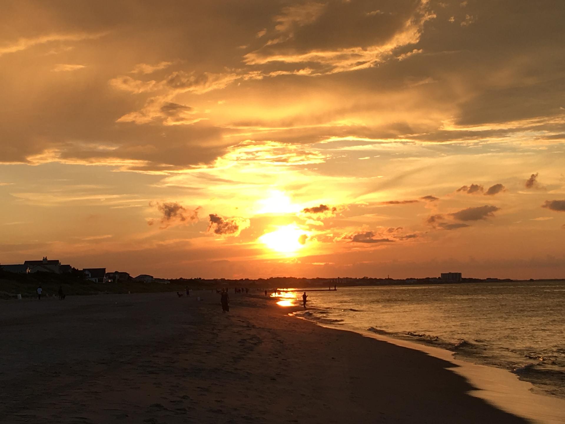 A vibrant golden sunset over a beach with people and ocean waves.