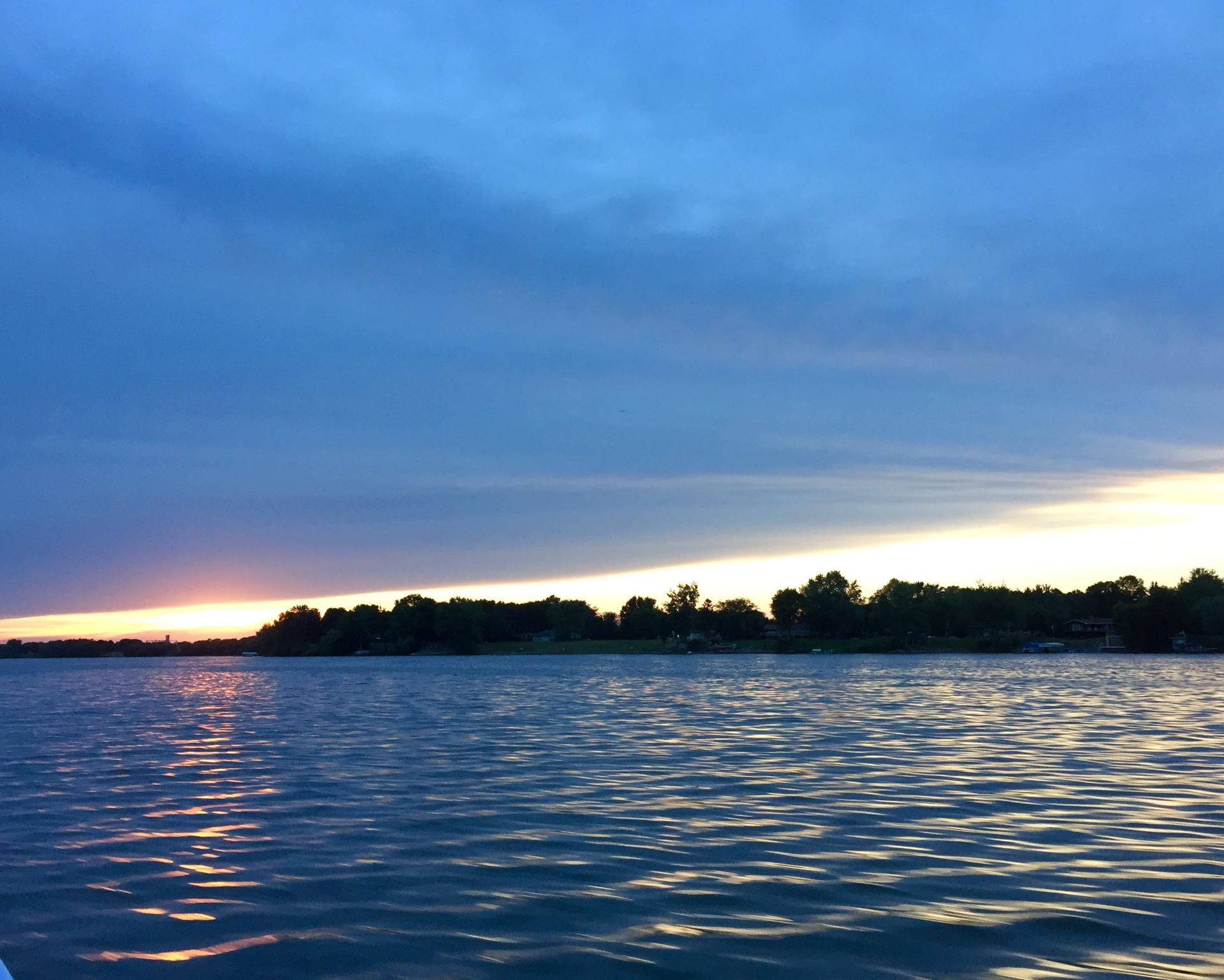 Calm lake at sunset with a dark blue sky and distant treeline.