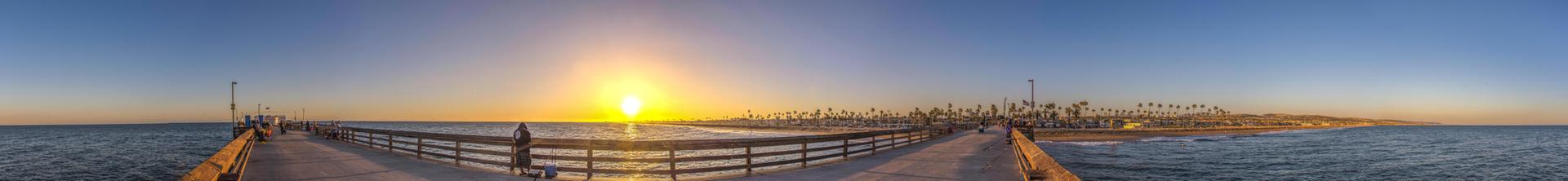 Panoramic sunset over the ocean from a pier, with a bright sun.