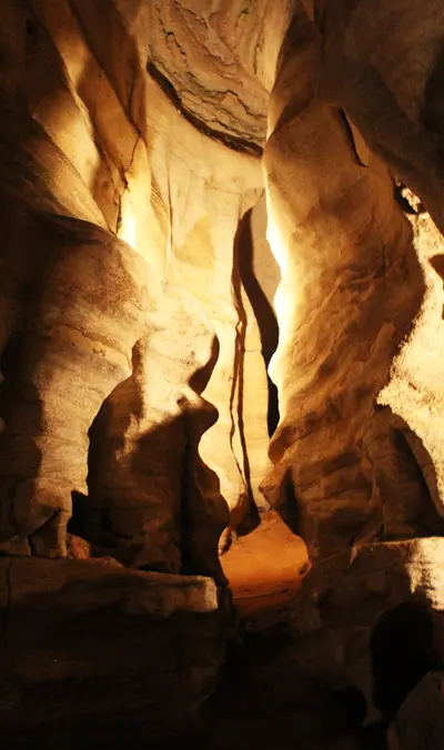 Warmly lit cave interior with intricate rock formations and a distant orange glow.