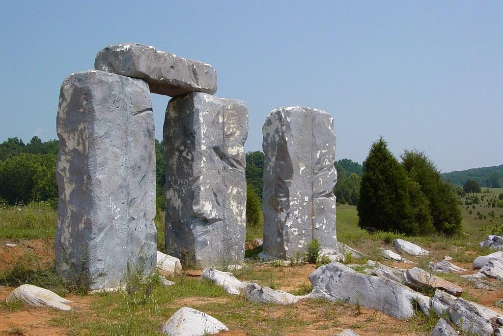 Large, weathered stone structures stand in a sunny, grassy field.