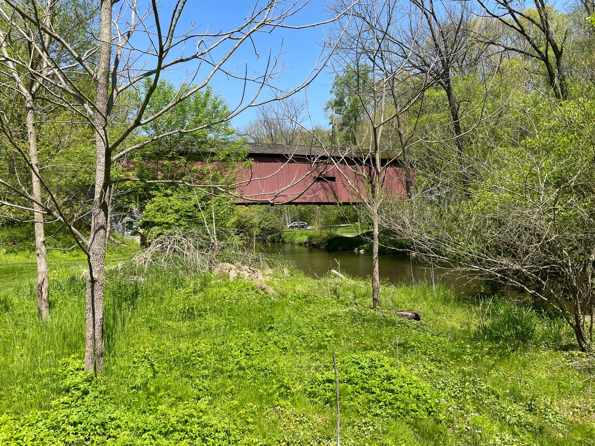 A red covered bridge spans a river, surrounded by vibrant green trees.