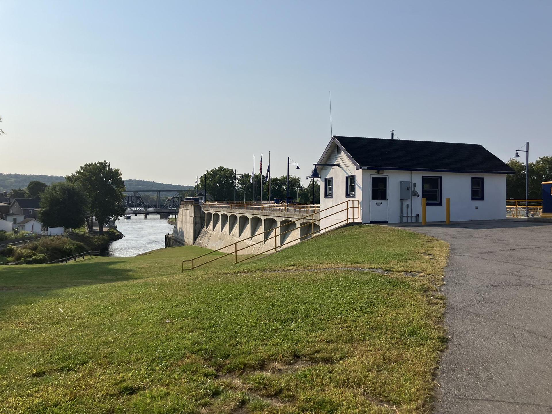 White building next to a concrete dam overlooking a river on a clear day.