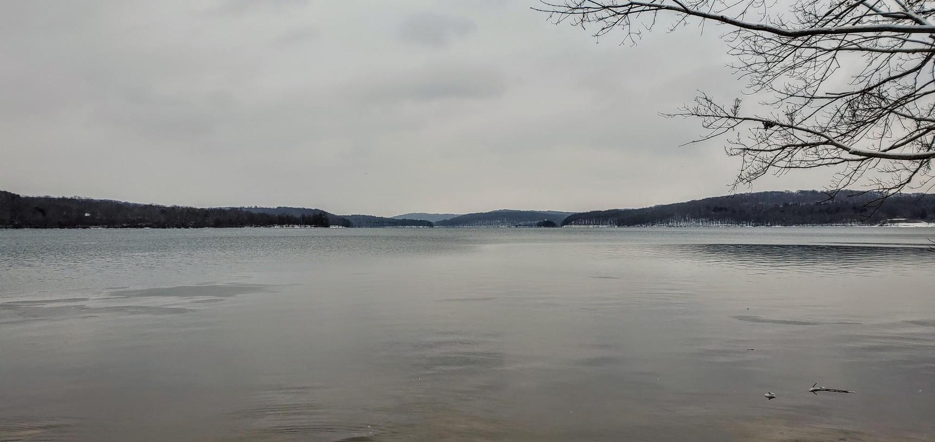 Wide, calm lake surrounded by snow-dusted hills under an overcast sky.