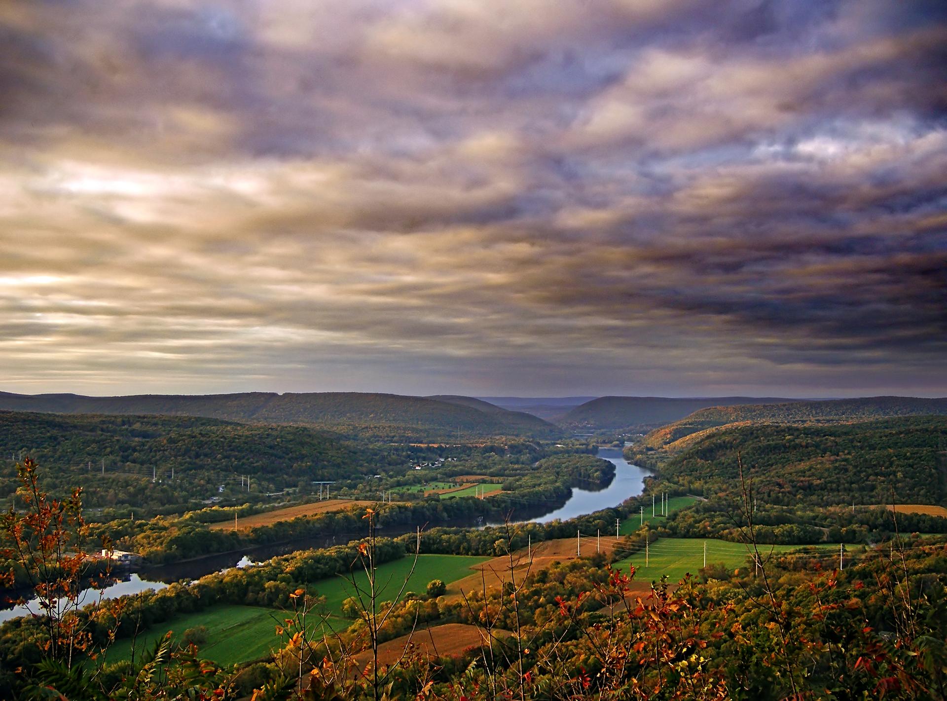 Expansive valley view with a winding river, green fields, and dramatic cloudy sky.