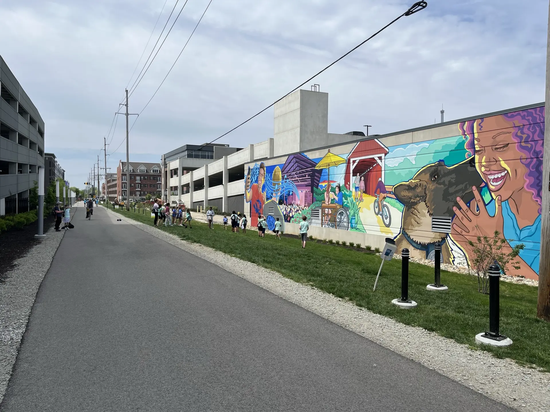 Paved path next to a vibrant mural with people walking on an overcast day.