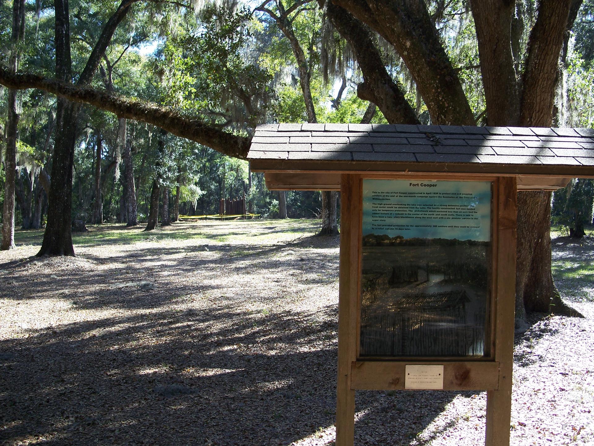 Wooden information sign in a sunny, wooded area with dappled light and trees.