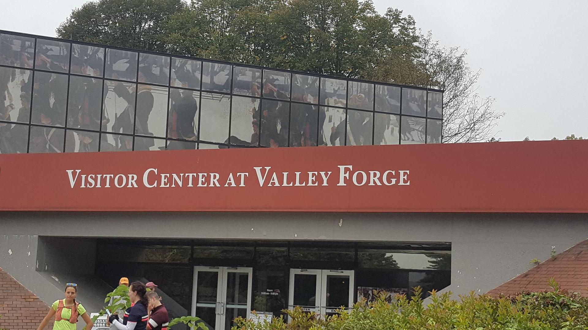 People stand outside a visitor center building with a red sign under an overcast sky.