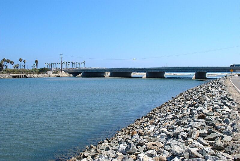 A wide river flows under a large concrete bridge on a sunny day.