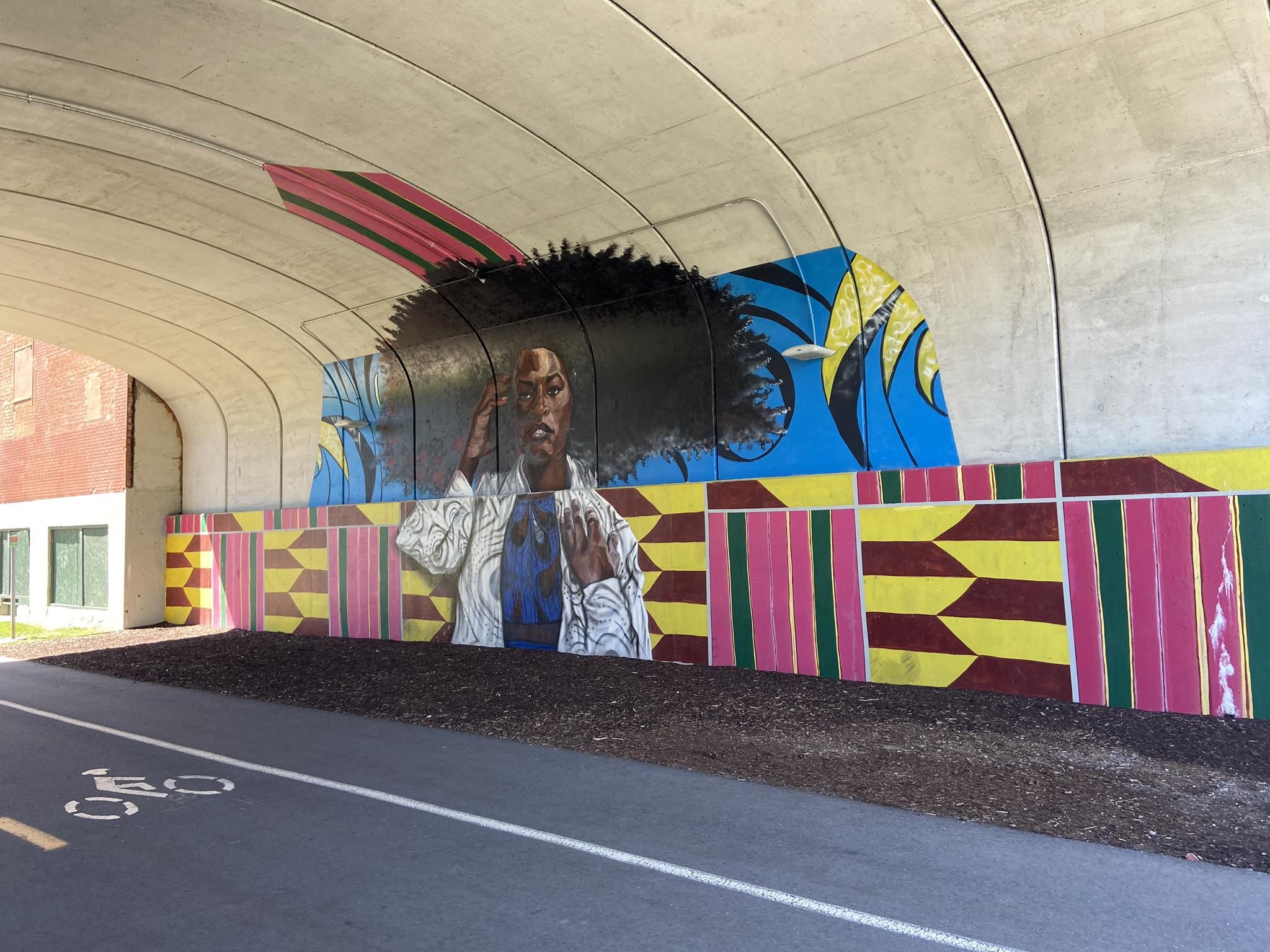 Colorful mural of a person under a concrete overpass with a bike path. - Dequindre Cut Greenway