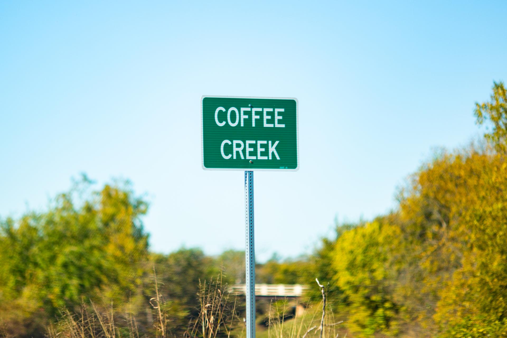 Green sign reading "COFFEE CREEK" against a bright blue sky and autumn trees.