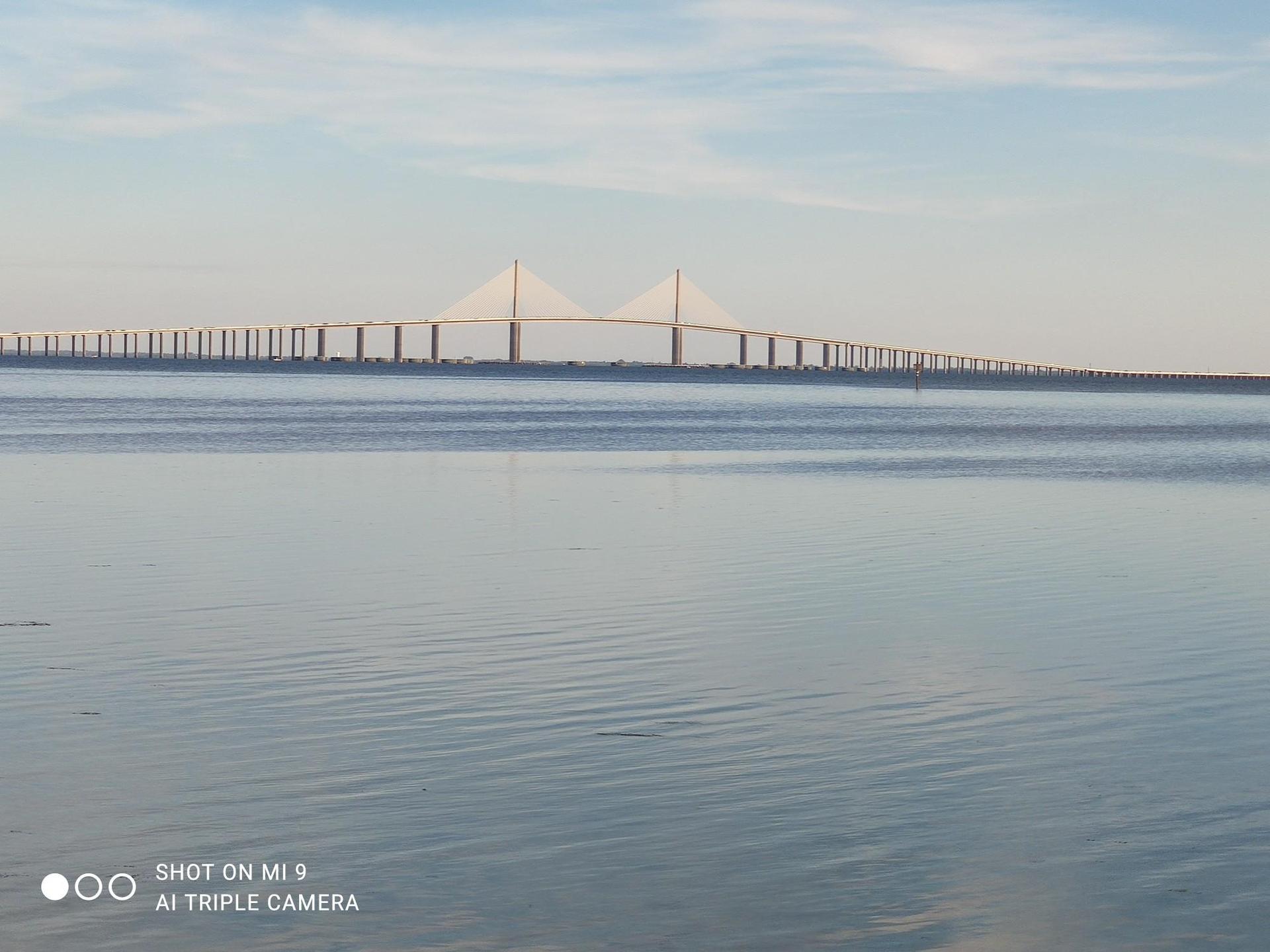 Long, modern bridge spanning calm water under a soft, clear sky.