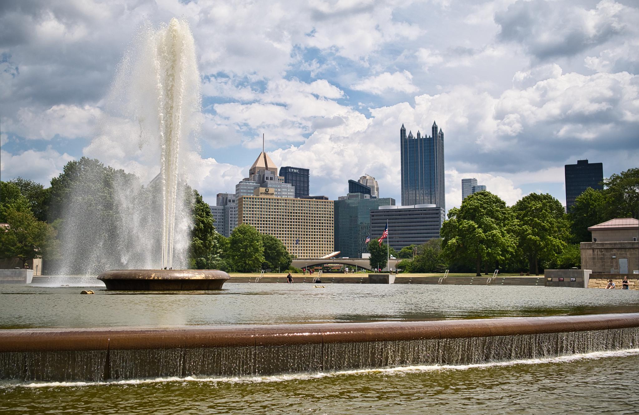 Large fountain spraying water with a city skyline in the background.
